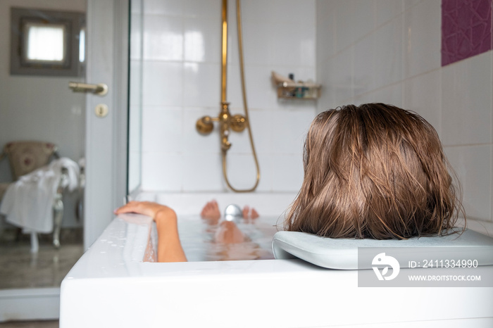 Close up shot of a young woman relaxing in a bath, resting her head on a bathtub pillow. Happy brunette female chilling in a bath of hotel room. Copy space, background.