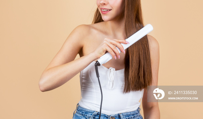 Beautiful girl using styler on her shining hair. Hairstyle. Beautiful smiling woman ironing long hair with flat iron. Happy woman straightening hair with straightener