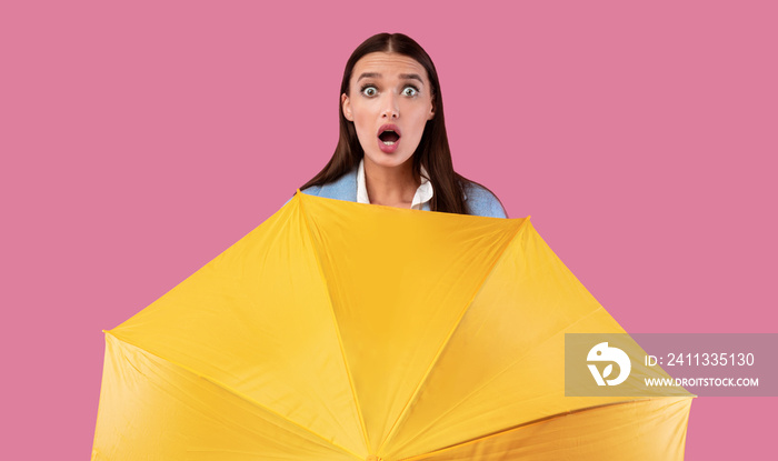 Portrait of shocked girl holding yellow umbrella at studio