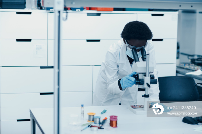 Scientist african american woman in face mask and gloves working in laboratory with electronic tech instruments and microscope. Research and development of electronic devices by color black woman.