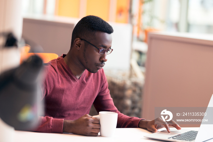 Handsome successful African American looking at the screen with serious face expression at modern startup office