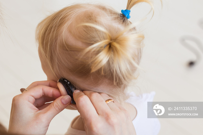 Hearing aid in baby girl’s ear. Toddler child wearing a hearing aid at home. Disabled child, disability and deafness concept.