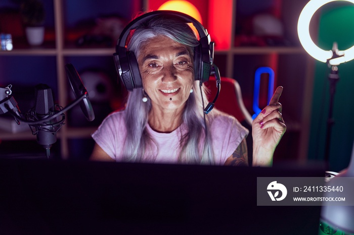 Middle age woman with tattoos playing video games wearing headphones smiling happy pointing with hand and finger to the side