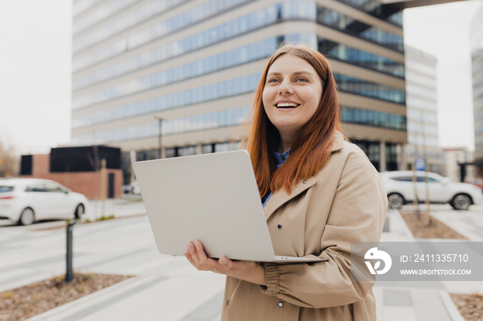 Caucasian businesswoman in fashion office clothes posing outside with a laptop. Successful woman working at laptop. Outdoor office. Business on the go concept.