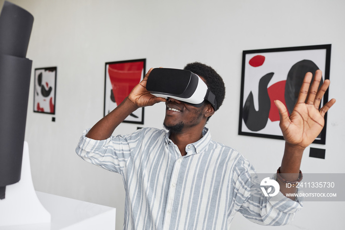Waist up portrait of smiling African-American man wearing VR gear while enjoying immersive experience at modern art gallery exhibition