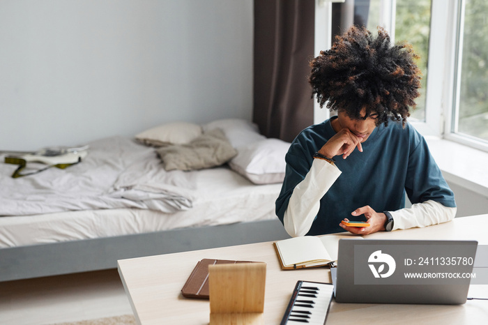 Minimal high angle portrait of African-American teenage boy using laptop while studying at home or in college dorm, copy space