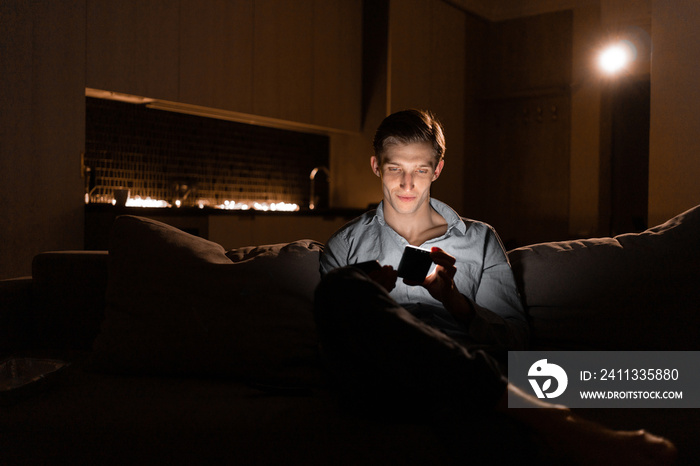 Young man with mobile phone at night. The user of the gadget creates a social network. Communication in the night chat. Internet addiction.