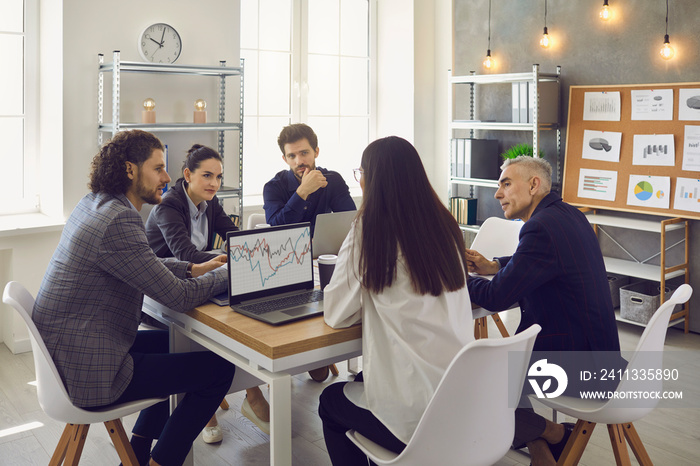 Company workers sitting around an office table in a corporate work meeting. Business team having a discussion, considering ways to increase sales and planning to enter a new market with a new product