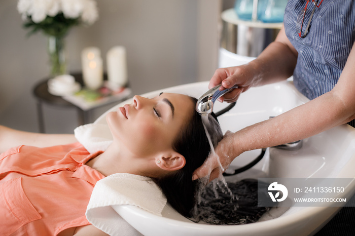 Top view of calm lady having water treatment in beauty salon. She is lying on armchair and putting head in sink while hairdresser is standing and washing it