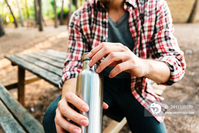 Young guy in the meadow with silver thermo bottle in aluminum.