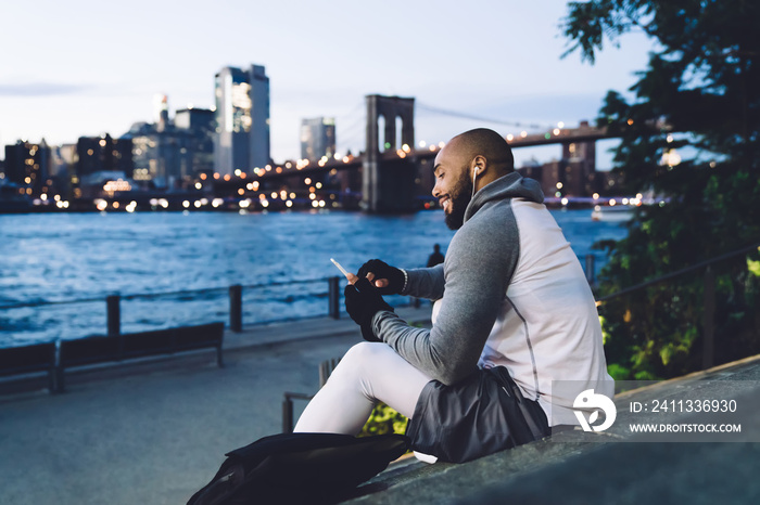 Strong black sportsman smiling with smartphone in hands