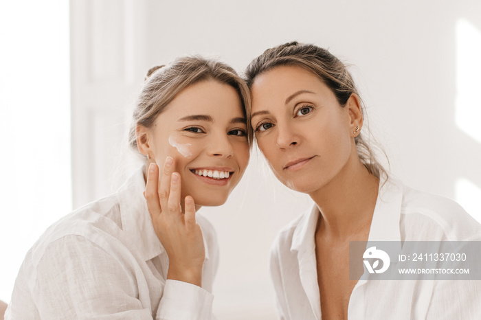 Close-up of beautiful caucasian young and adult woman looking at camera on white background. Blonde girls with collected hair in shirts. Rituals of female beauty, concept