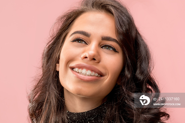 Beautiful young woman with teeth braces on pink