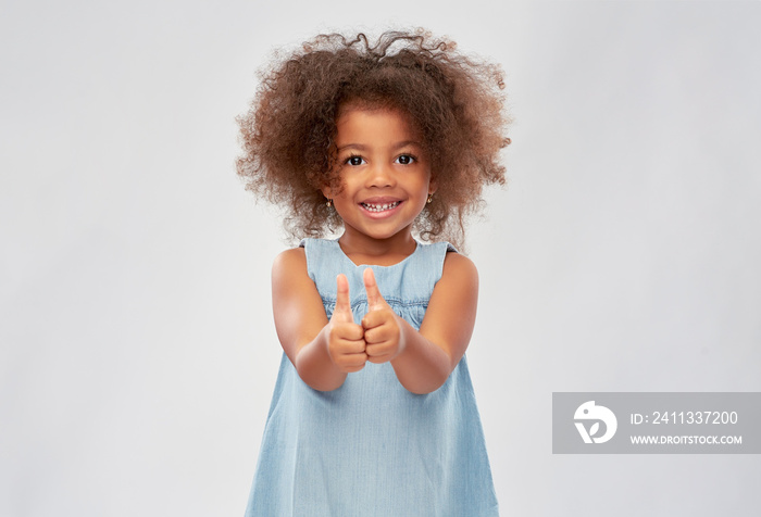 childhood, gesture and people concept - happy little african american girl showing thumbs up over grey background