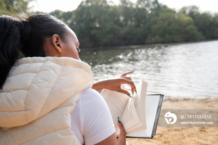 Rear view of woman reading book on lakeshore