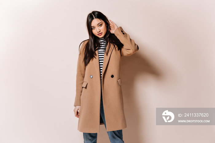 Beautiful Asian woman looking confidently into camera. Girl in beige coat posing on isolated background