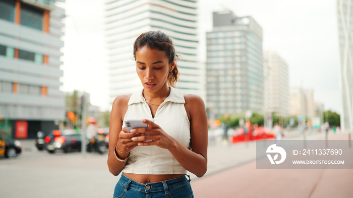 Clouse-up, cute tanned woman with ponytail wearing white top looking up at street signs and map trying to find her way using cellphone. Girl using map application outdoors