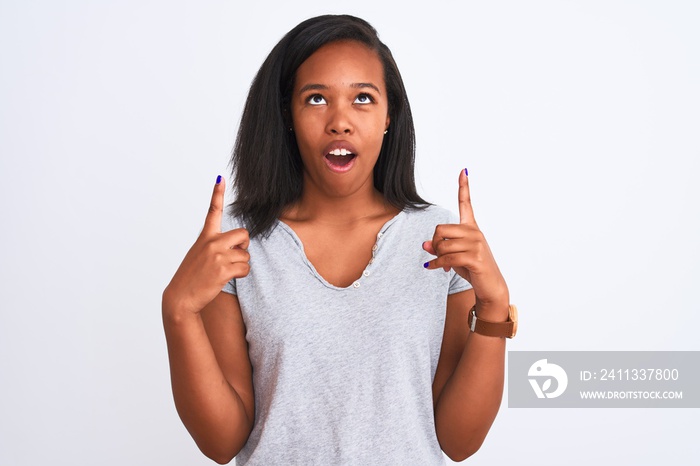 Beautiful young african american woman wearing casual t-shirt over isolated background amazed and surprised looking up and pointing with fingers and raised arms.