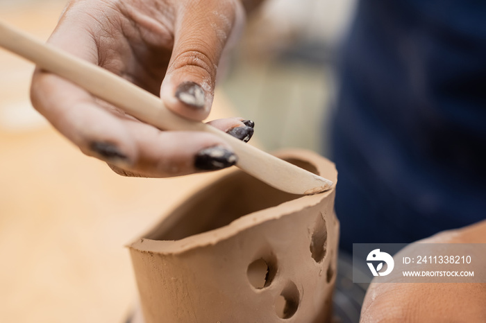 Close up view of african american craftswoman using tool while making clay product in workshop.