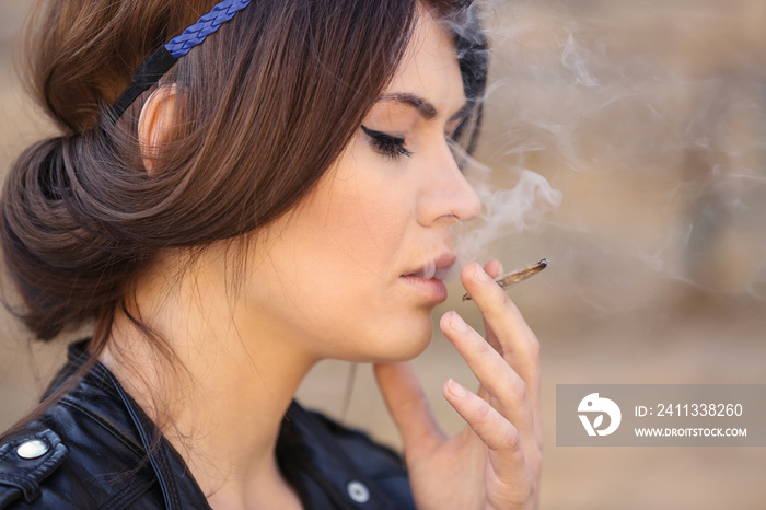 Beautiful young woman smoking weed outdoors