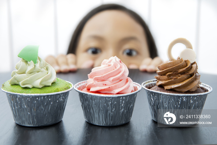 Little girl is peeping tasty cupcakes