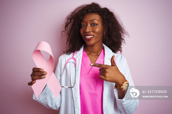 Young african american doctor woman holding cancer ribbon over isolated pink background very happy pointing with hand and finger