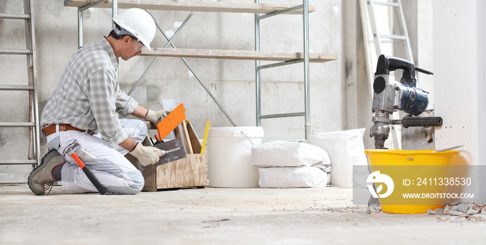 plasterer man construction worker work with tool box wear gloves, hard hat and protection glasses at interior building site with scaffolding. bucket, sacks and jackhammer