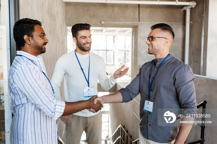 business, gesture and partnership concept - happy businessmen name tags making handshake at office