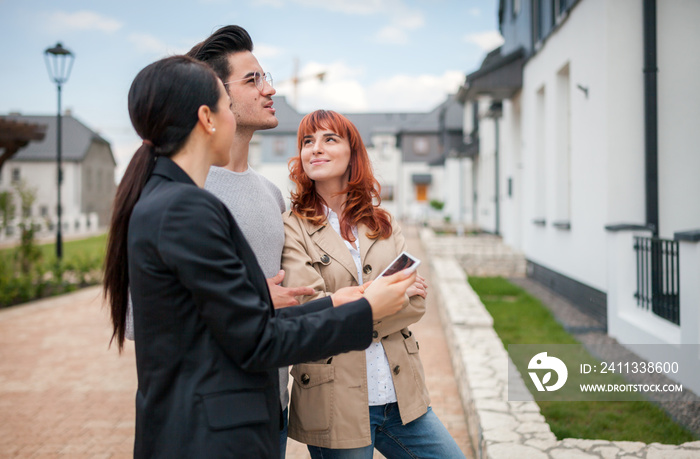 Young couple with real estate agent visiting house for sale in residential area