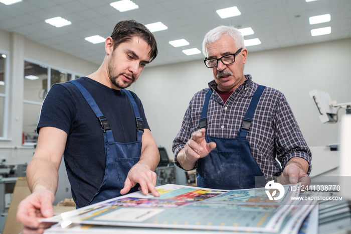 Experienced senior worker in glasses explaining young man how to estimate print quality during his internship