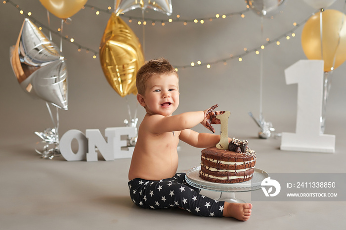 Smash cake party. Little cheerful birthday boy with first cake. Happy infant baby celebrating his first birthday. Decoration and photo zone for first year. One year baby celebration. Grey decor.