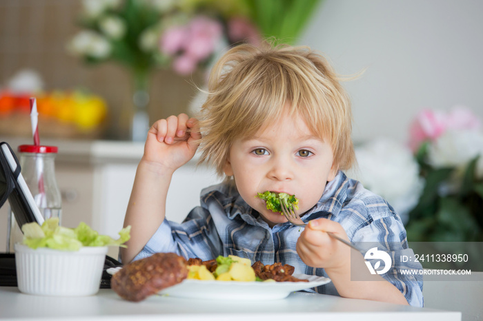 Little toddler child, blond boy, eating boiled vegetables, broccoli, potatoes and carrots with fried chicken meat at home