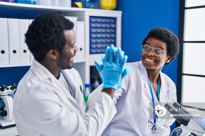 African american man and woman scientists high five with hands raised up at laboratory