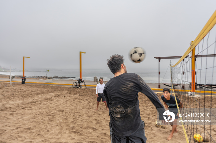 Man jumping to kick a ball during a footvolley match on the beach