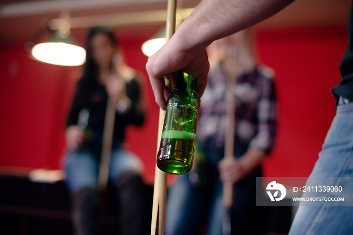 Man is holding beer and billiard stick