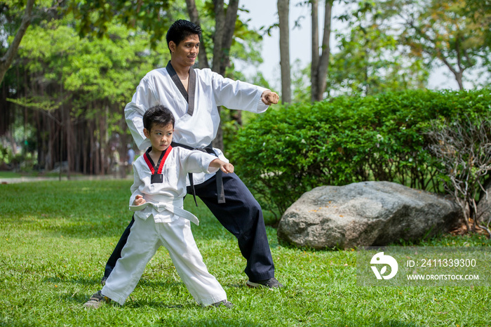 father coach is training his son boy taekwondo in green park .children kid and teacher master trainer are learning karate outdoor in the nature park .martial arts