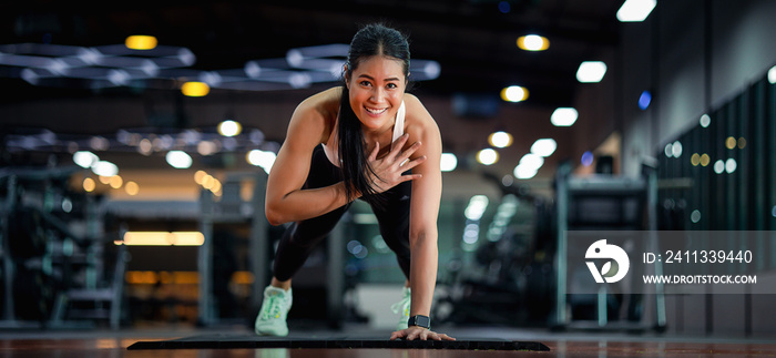 Happy beautiful young asian woman doing push ups exercise with one hand in fitness gym.