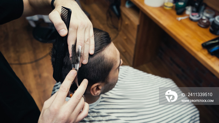 Overhead view of barber cutting hair of man in blurred hairdressing cape in barbershop.