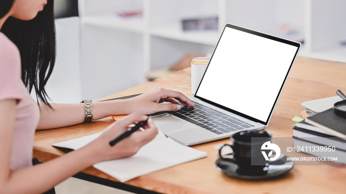 Young woman using laptop computer and writing on notebook paper in library room.