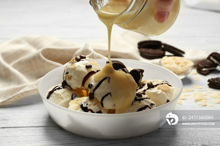 Pouring sauce onto delicious dessert with ice cream in bowl