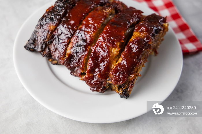 Oven-baked barbecue ribs with sauce on a white plate with a red checkered picnic napkin for a family barbecue