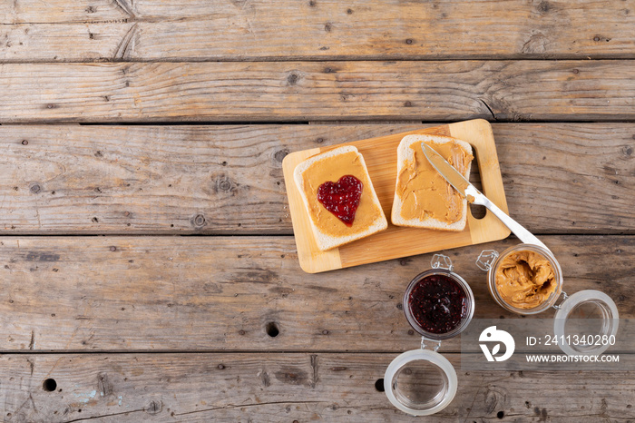 Overhead view of open face peanut butter and jelly sandwich on serving board with jars at table