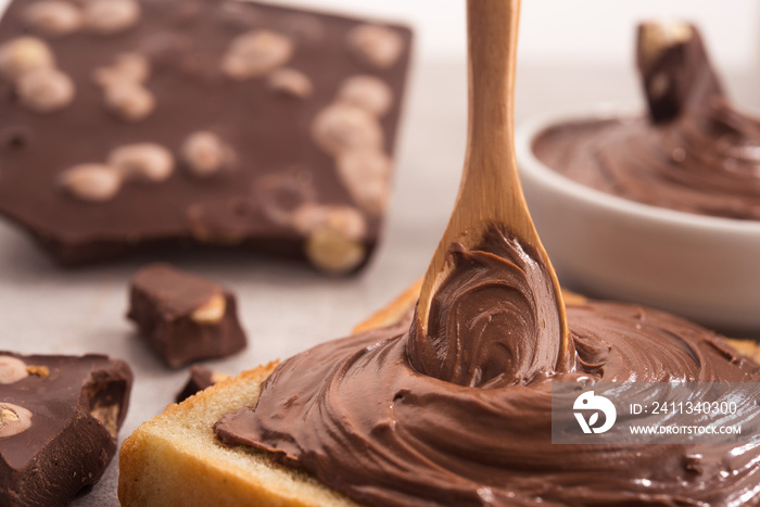 Chocolate spread on slice of bread with spoon, melted cream white bowl