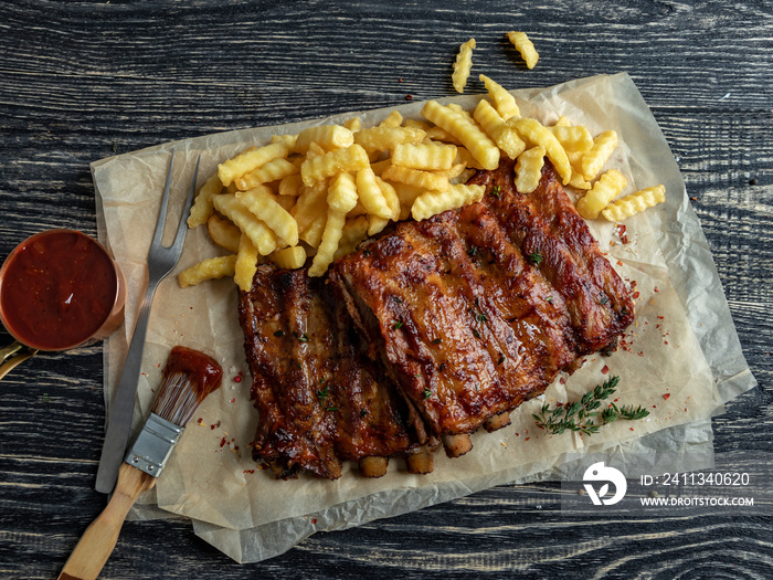 grilled roast pork ribs with sauce , french fries, spices, wooden background