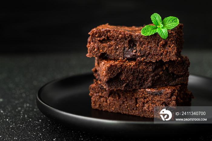 Dark chocolate and cocoa brownie fudge cakes dessert with mint against black and grey stone background