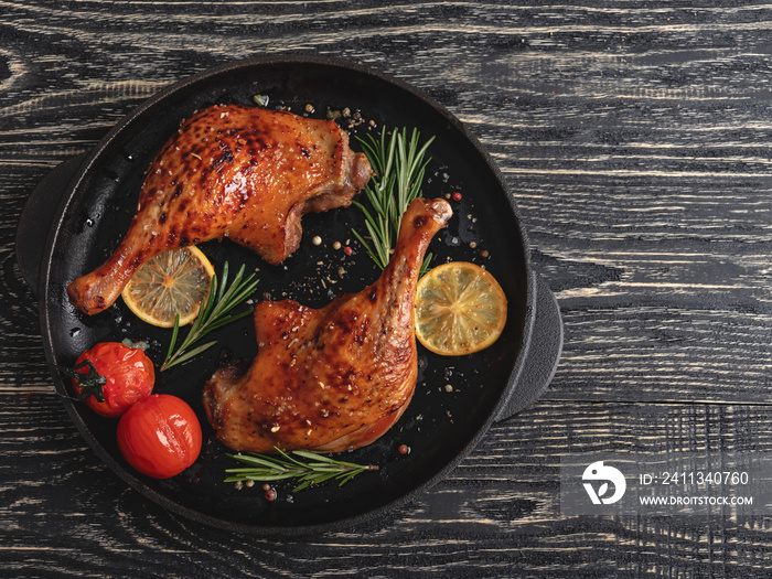 Juicy grilled duck legs with with tomato and lemon in a fry pan , black surface, close up