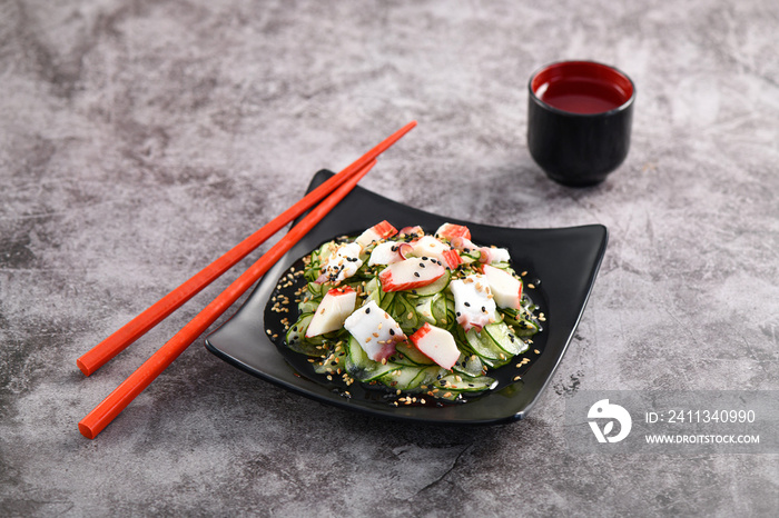 Crab and cucumber salad served on dark dish. Sunomono, slim cucumber slices. Studio shoot.