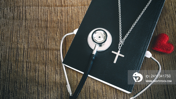 Stethoscope and cross on bible with red heart , concept of christian for treatment.