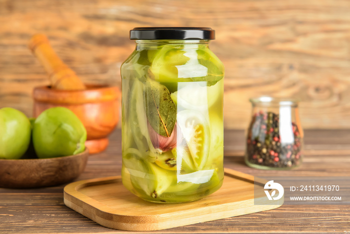 Jar with canned green tomatoes on wooden background