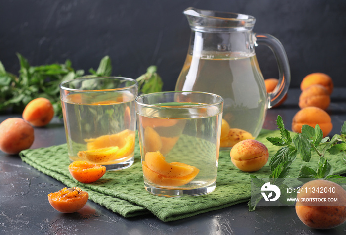 Homemade apricot compote in two glasses and jug on gray background